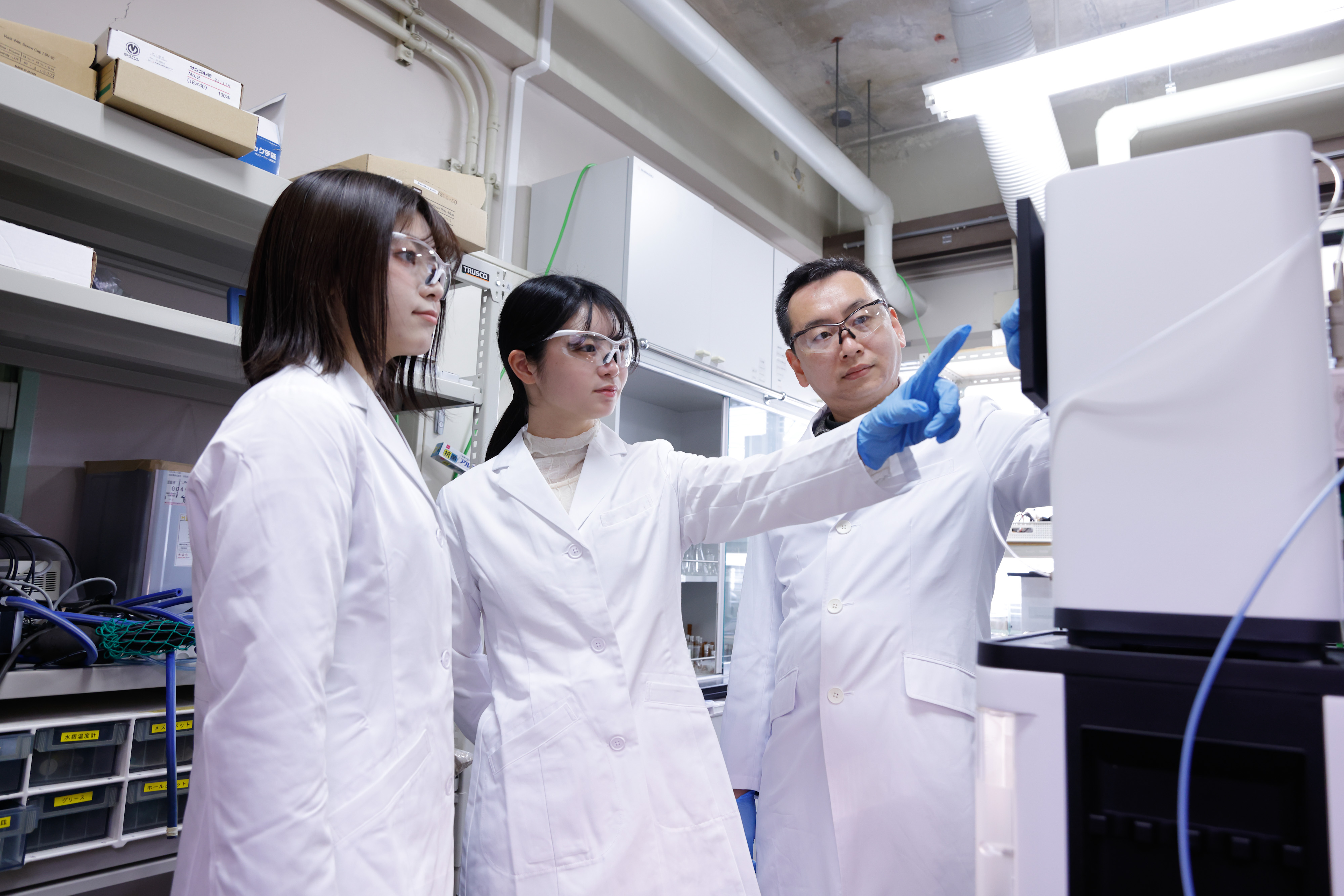 写真:女子学生3人が教員から実験の説明を受けている